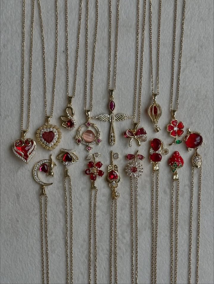 “Gold and red enamel pendant necklaces displayed in a row featuring hearts, flowers, moons and cross designs”